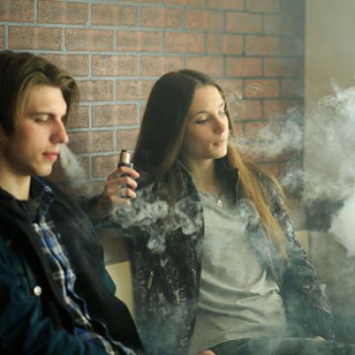 Two young people smoking e-cigarettes. Adobe
